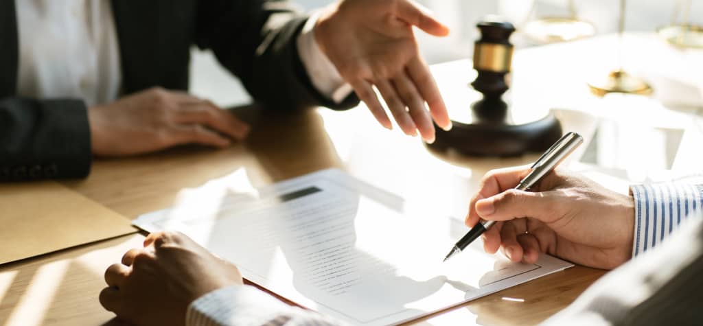 Two professionals are discussing a document on a table, with one hand gesturing and the other writing with a pen.