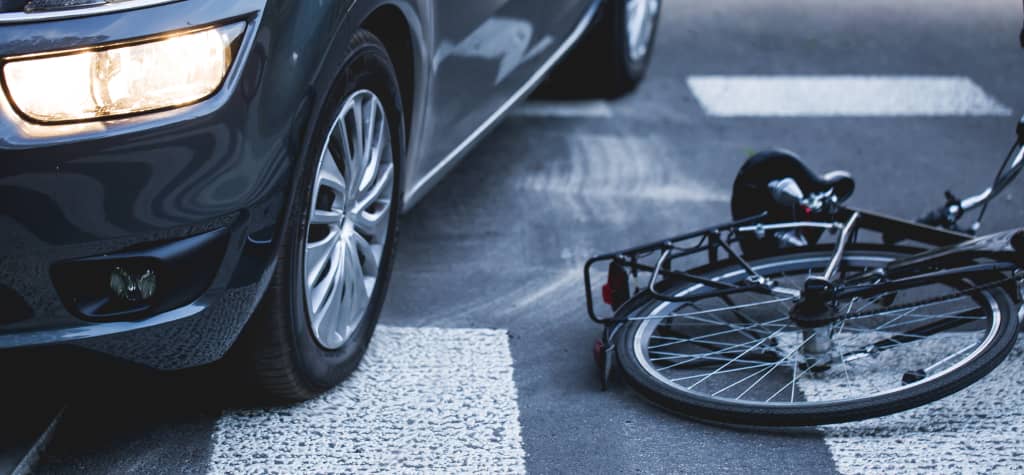 A car's tire rests on a crosswalk, beside an overturned bicycle, highlighting a recent accident scene on the road.