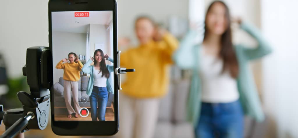A smartphone on a tripod captures two dancers performing in a home setting, while a timer counts down on the screen.