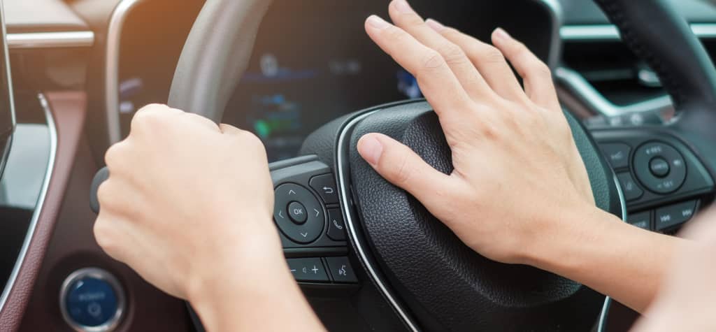 A close-up of hands gripping a car steering wheel, highlighting controls and a dashboard in the background.