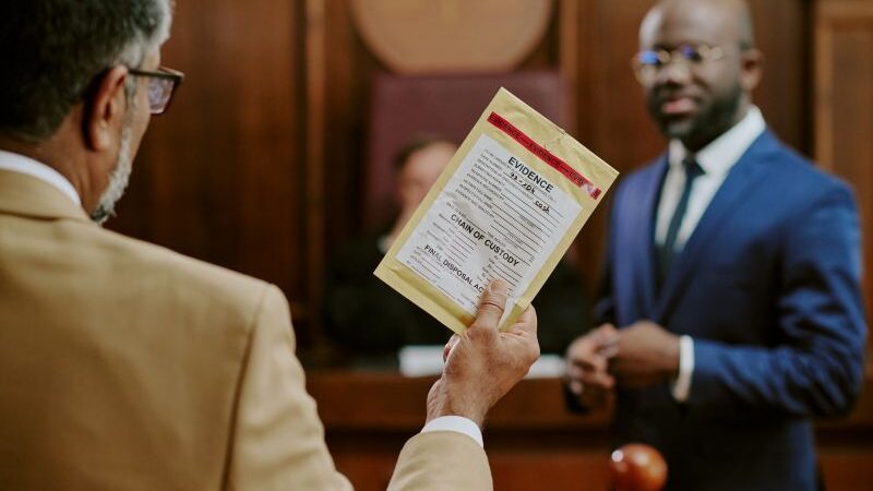 Attorney in court holding up evidence next to another attorney and judge.
