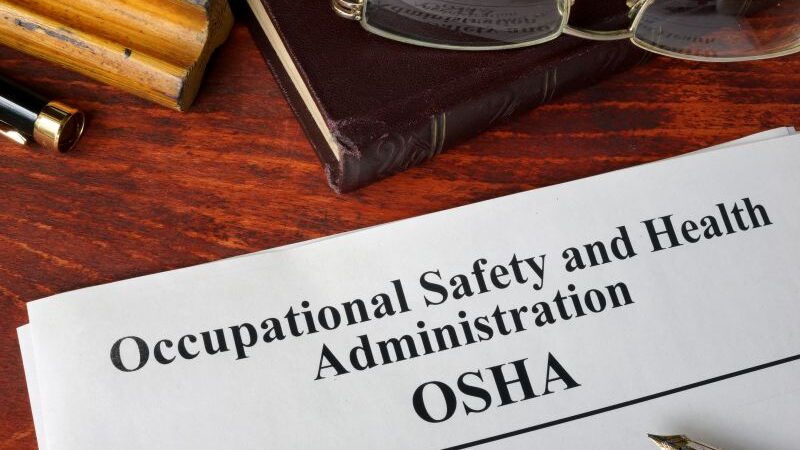 Occupational Safety and Health Administration OSHA paperwork sitting on a desk with pens, a binder and eyeglasses.