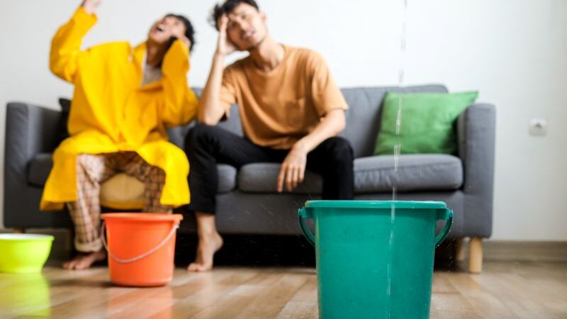 Couple sitting on a couch with buckets on the floor collecting dripping water.