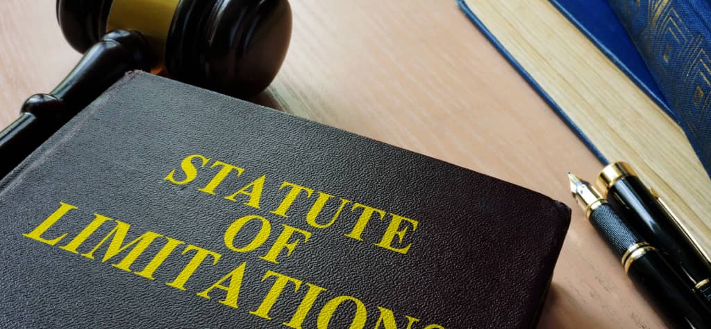A gavel rests beside a book titled "Statute of Limitations," with a classic pen and another legal book in the background.