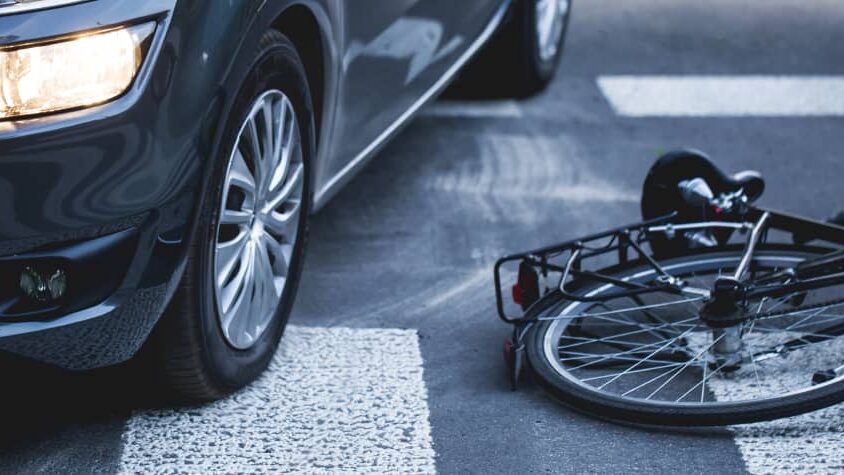 A car's tire rests on a crosswalk, beside an overturned bicycle, highlighting a recent accident scene on the road.